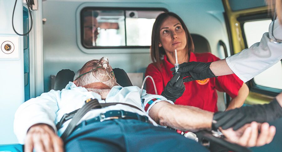 Mężczyzna po ciężkim zawale serca leży w karetce, ratownik medyczny przeprowadza czynności ratujące
