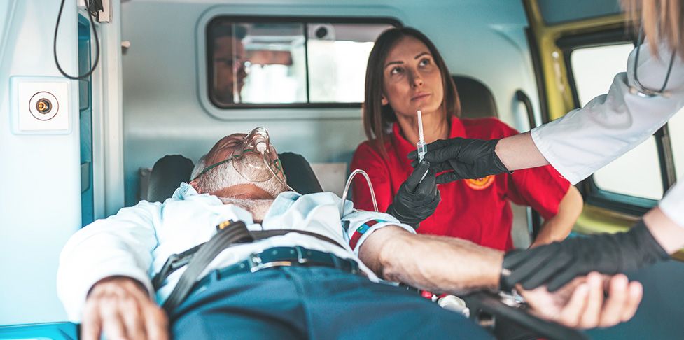 Mężczyzna po ciężkim zawale serca leży w karetce, ratownik medyczny przeprowadza czynności ratujące