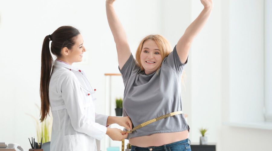 Młoda lekarka mierzy talię kobiety z nadwagą za pomocą centymetra w klinice