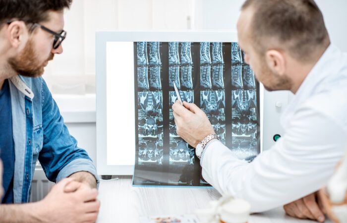 Mężczyzna podczas konsultacji medycznej z lekarzem ortopedą patrzącym na zdjęcie z tomografii komputerowej