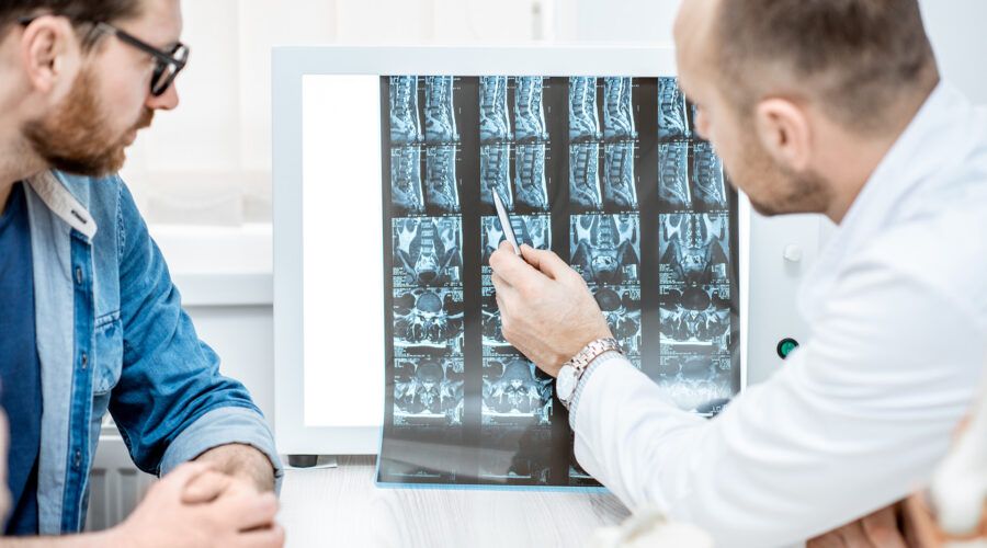 Mężczyzna podczas konsultacji medycznej z lekarzem ortopedą patrzącym na zdjęcie z tomografii komputerowej