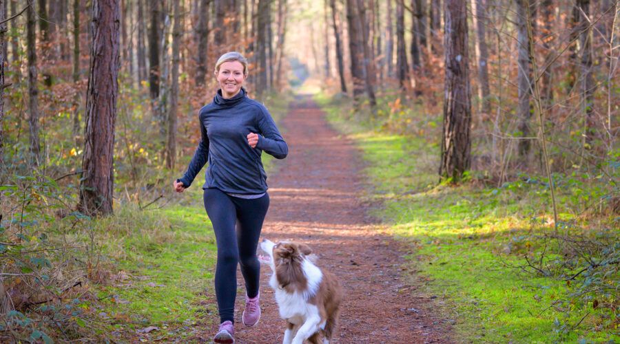 Kobieta w średnim wieku biegnie przez las z psem