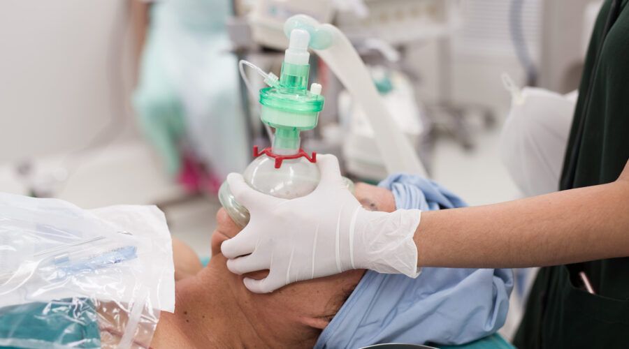 Lekarz podaje leżącej na stole operacyjnym pacjentce tlen przed wprowadzeniem w stan znieczulenia ogólnego