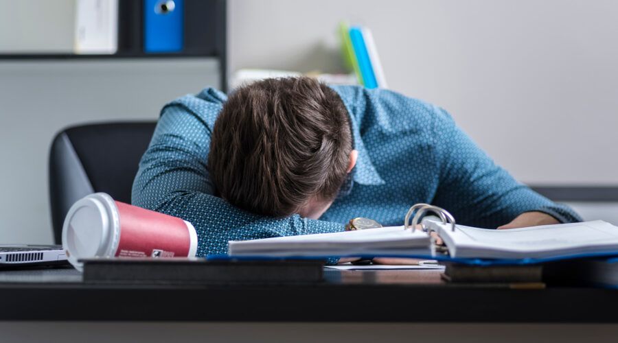 Zmęczony mężczyzna śpi w pracy z głową oparta na biurku